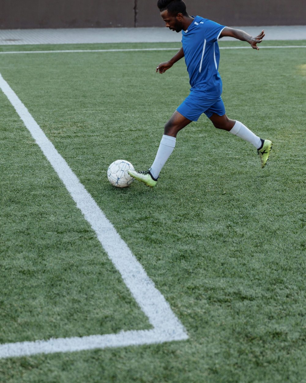A young male soccer player kicks the ball on a green field, showing athletic skills.