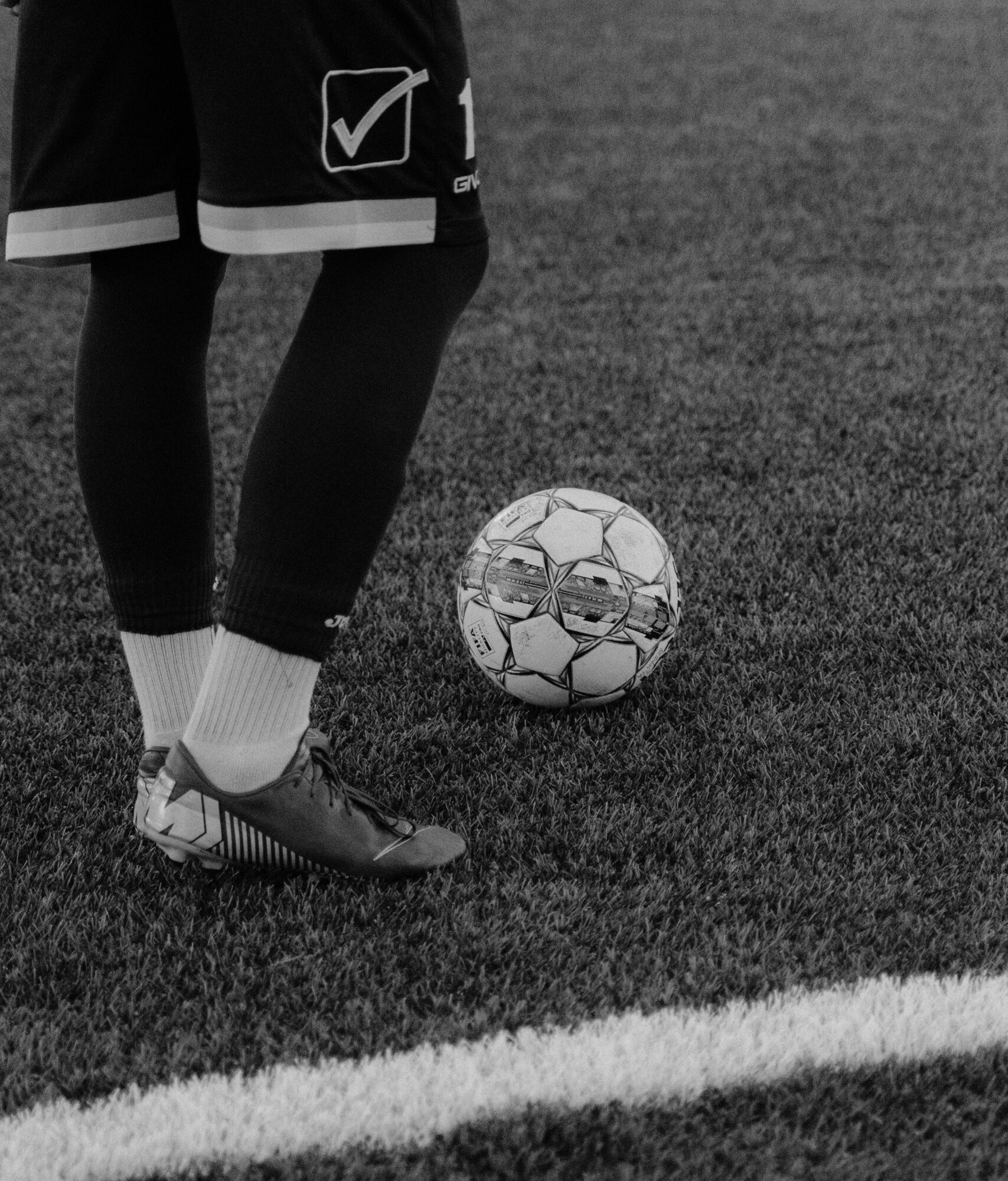 Black and white image of a soccer player preparing to kick the ball on a grass field.